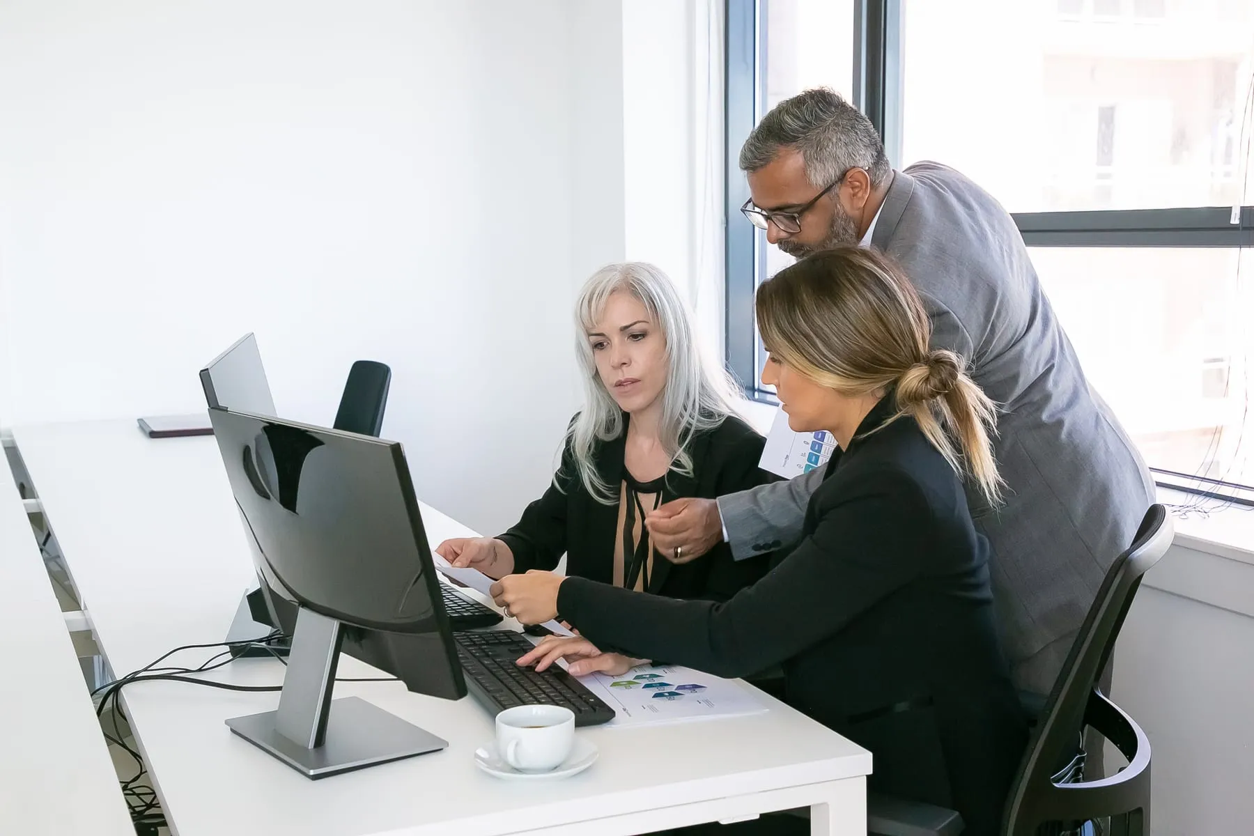 Business team three analyzing reports sitting workplace with monitors together holding reviewing discussing papers with charts copy space